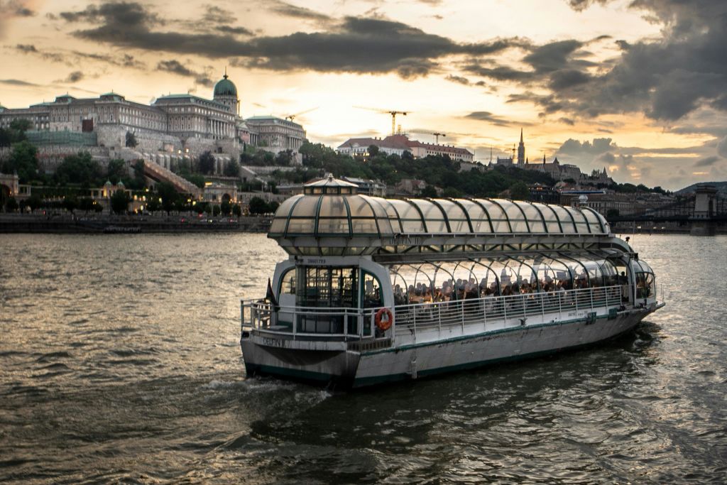 역사적인 건물과 석양을 배경으로 강가에 유리 돔형 보트가 있습니다.