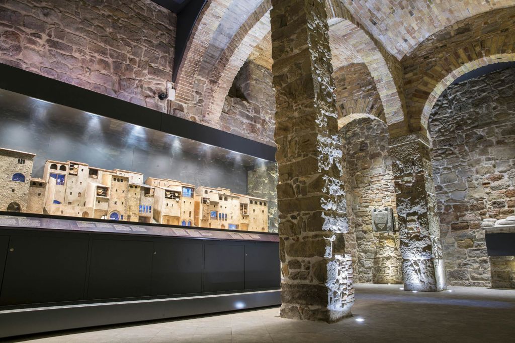 정교한 벽돌과 기둥이 있는 조명이 밝은 석조 아치형 방에 전시된 유서 깊은 건물의 스케일 모델입니다.