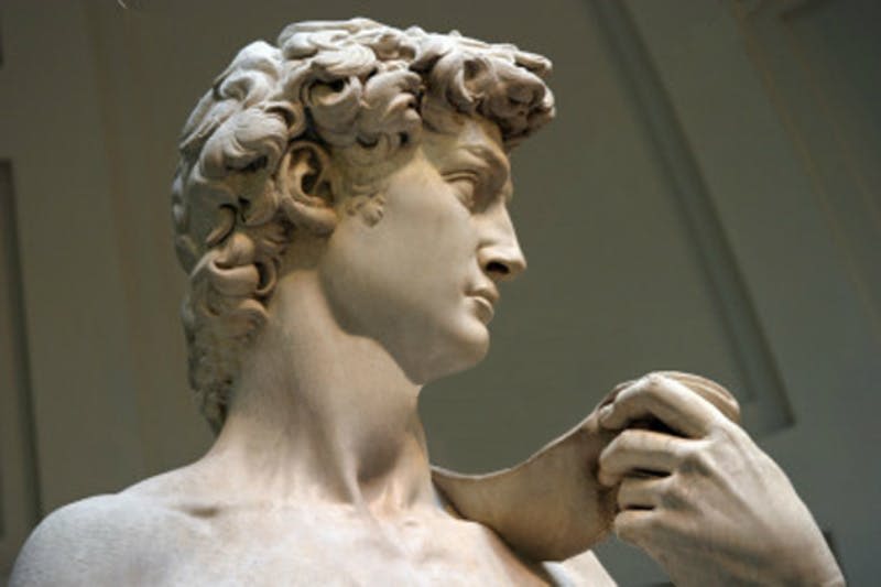 어깨 너머로 물건을 들고 옆을 바라보며 곱슬머리를 한 남성의 대리석 동상. 배경은 중립적입니다.