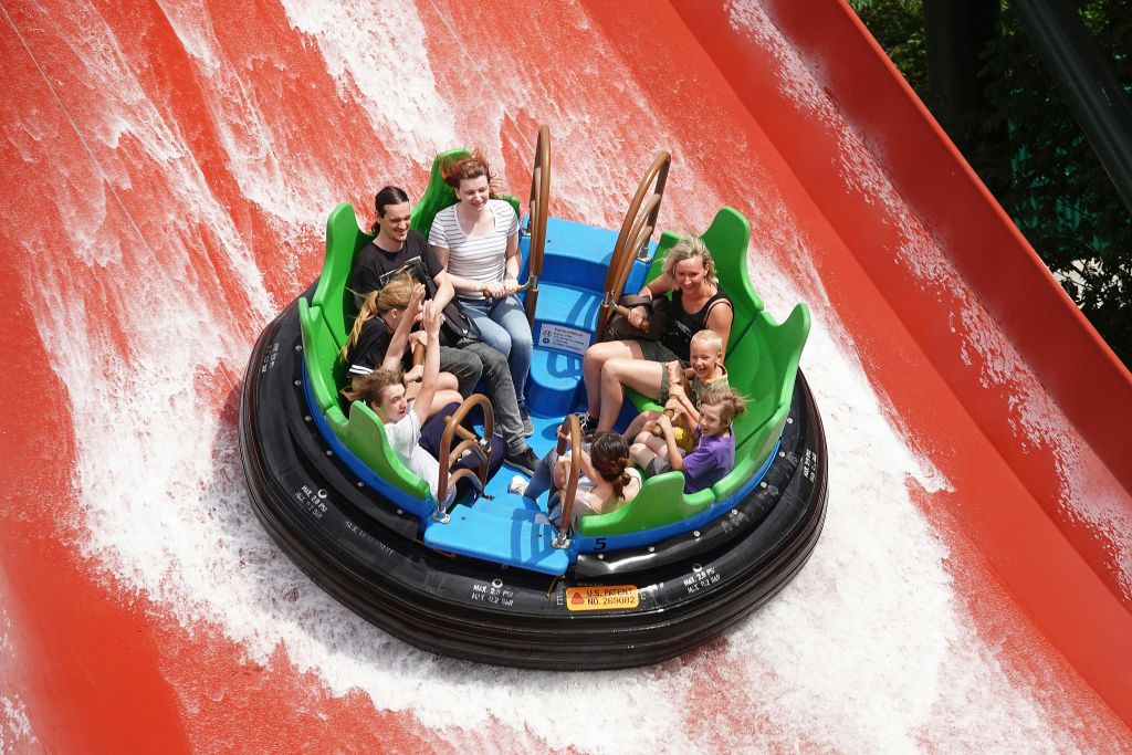 한 무리의 사람들이 원형의 물을 타고 물이 튀는 붉은 미끄럼틀을 타고 내려갑니다.