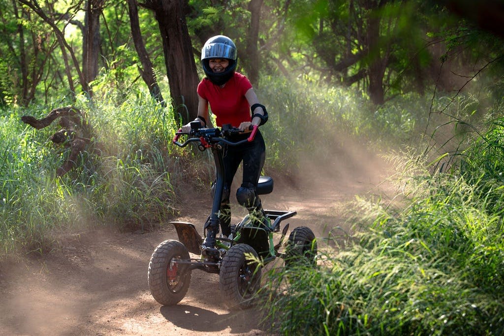 숲 속 흙길에서 전지형 전동 스쿠터를 타고 보호 장비와 헬멧을 착용한 사람.