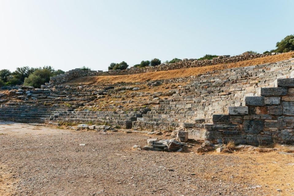 화창한 날 희박한 초목으로 둘러싸인 풍화 석재가 줄지어 있는 고대 석재 원형극장.