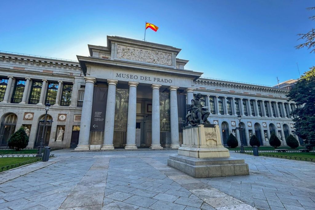 마드리드의 프라도 미술관 정문에는 전경에 동상이 있고, 그 위를 날아다니는 스페인 국기가 있습니다.