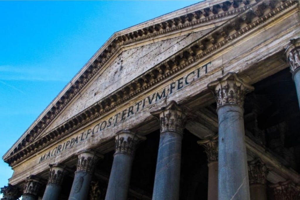이 이미지는 로마 판테온의 앞면 페디먼트와 기둥을 보여주며, 프리즈에 라틴어가 새겨져 있습니다.