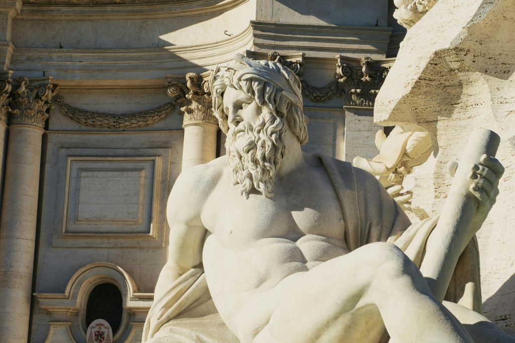 더 큰 화려한 건축 구조의 일부인 드레이프 천으로 장식된 수염이 있는 남자의 상세한 대리석 조각상을 클로즈업으로 볼 수 있습니다.