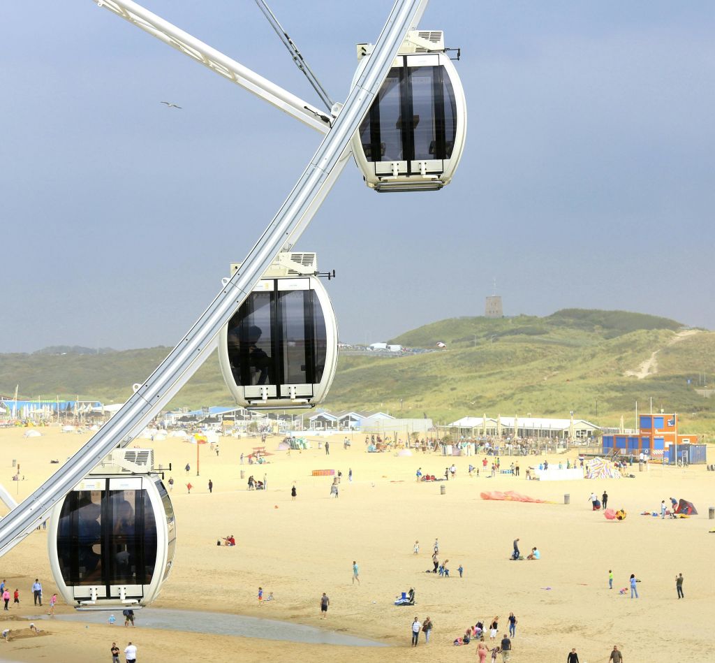 언덕과 건물을 배경으로 모래 해변을 거닐며 휴식을 취하는 사람들이 있는 전경의 대관람차 통나무집.