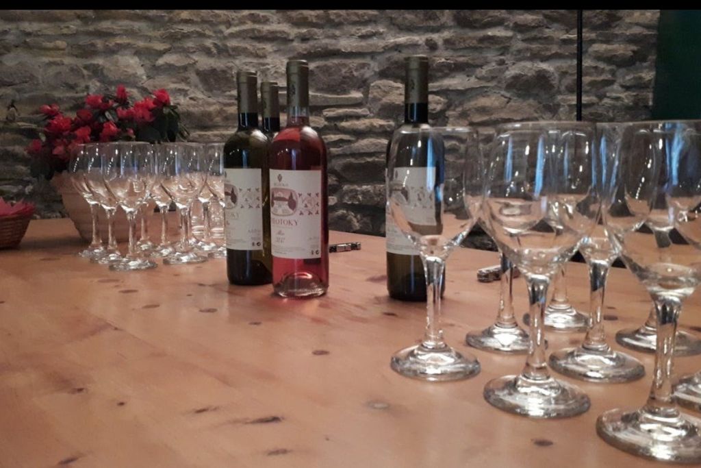 돌담 앞 나무 테이블에 놓인 와인병과 여러 개의 와인잔.