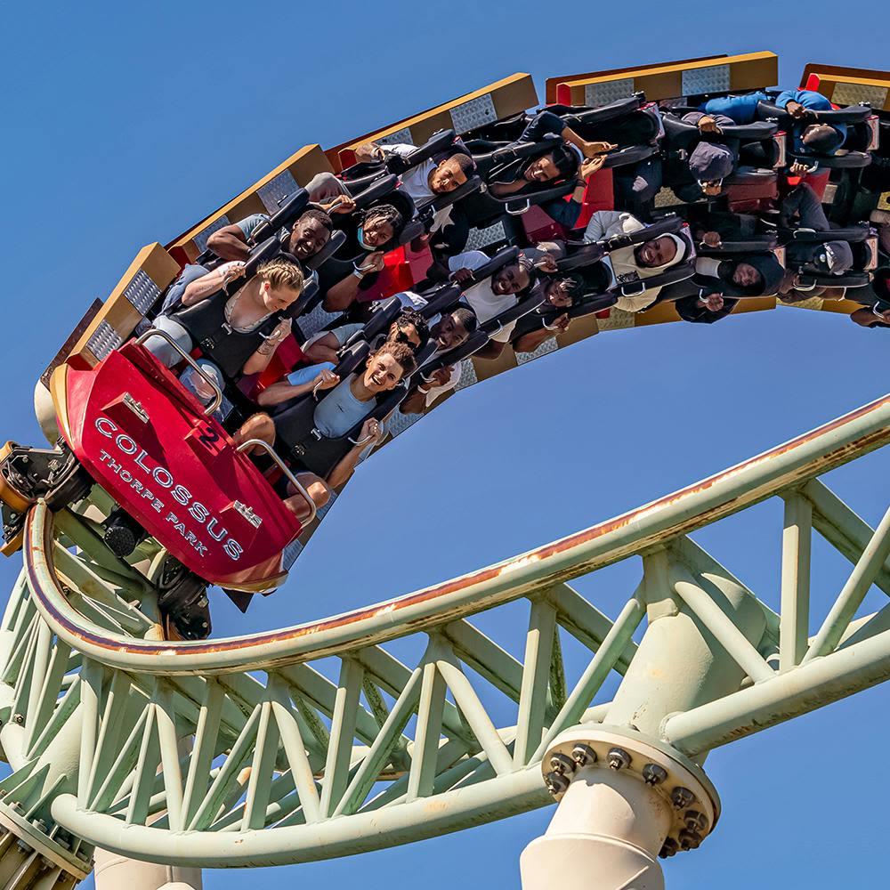 맑고 푸른 하늘 아래서 흥분된 표정으로 거꾸로 고리를 타고 있는 콜로서스 롤러코스터를 타는 사람들.