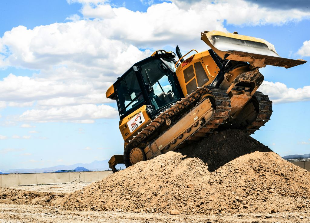 부분적으로 흐린 하늘 아래 흙먼지를 밀어 올리는 불도저.