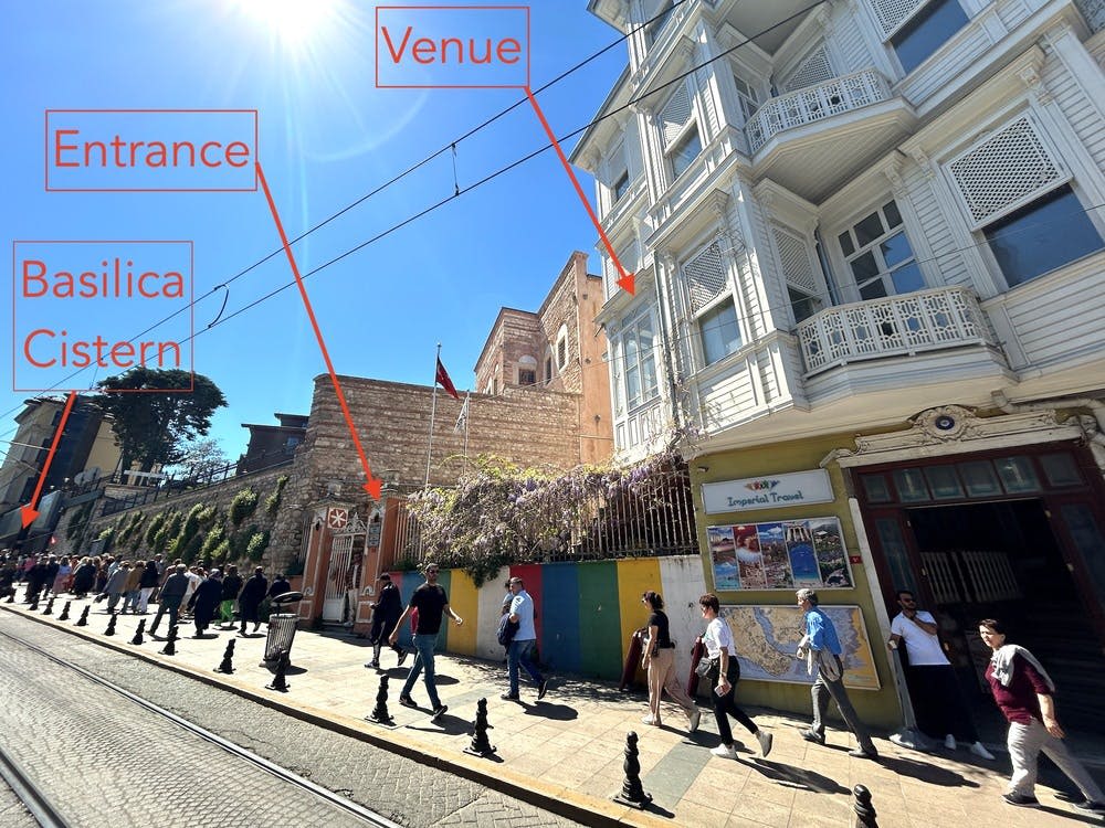 화창한 날 자갈길을 따라 걷는 사람들로, 역사적인 건물과 "장소" 라고 쓰인 표지판이 위를 가리키고 있습니다.