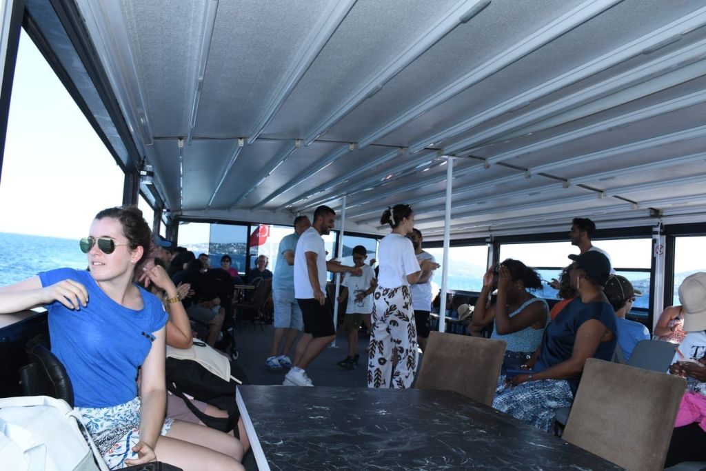 창문을 통해 바다가 보이는 지붕이 있는 보트 데크에 사람들이 앉아서 서 있습니다.