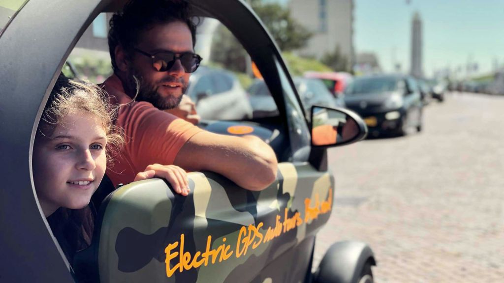 선글라스를 착용한 남성과 어린이가 "전기 GPS" 가 적힌 카모 무늬 차량의 창문을 내다보고 있습니다.