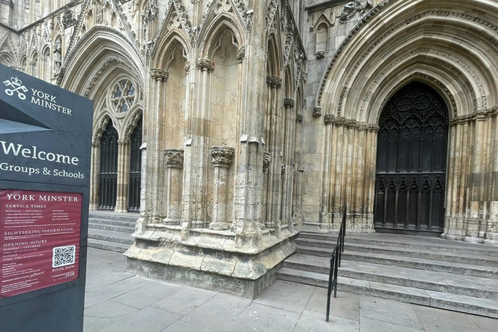 뾰족한 아치, 정교한 조각, 어두운 나무 문으로 이어지는 계단이 있는 화려한 고딕 성당 입구.