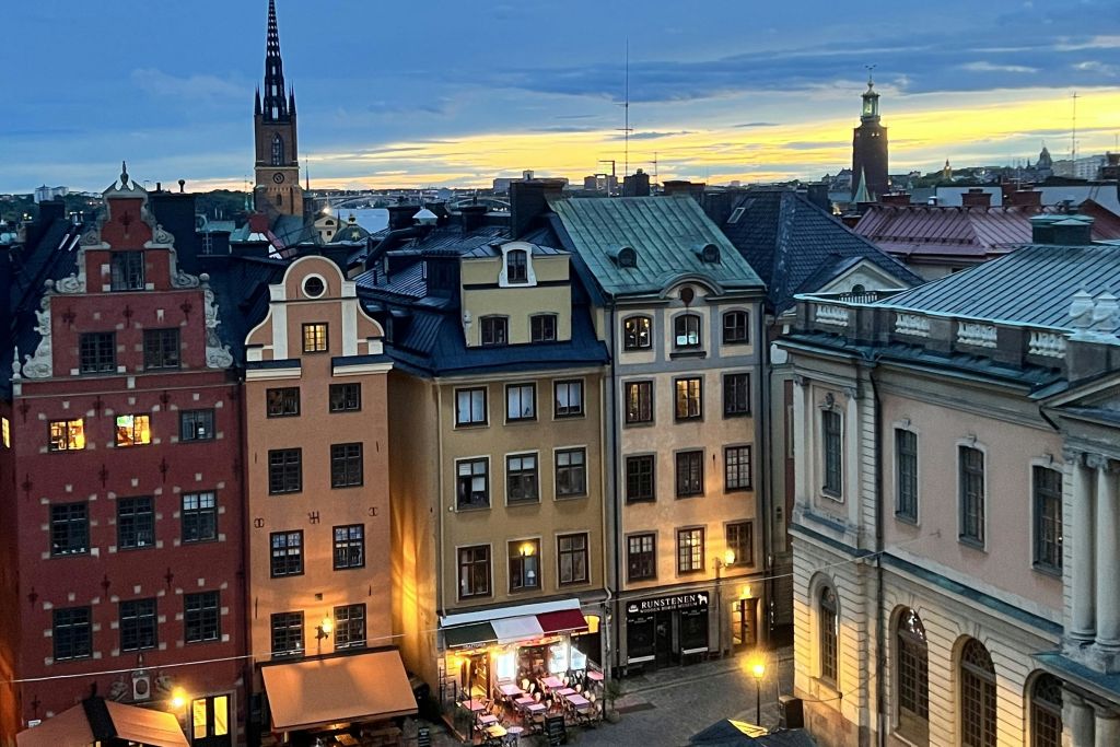 화려한 건물, 작은 야외 카페, 빛나는 하늘 아래 먼 교회 가파도가 있는 매력적인 유럽 거리의 저녁 풍경.