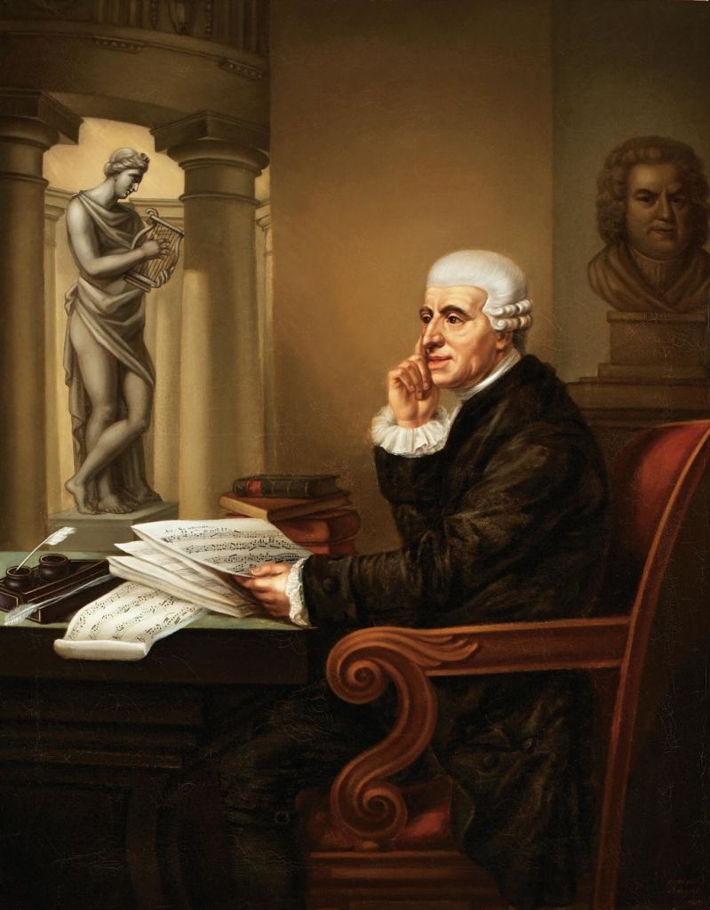 흰 머리를 한 노인이 악보가 있는 책상에 앉아 사려 깊은 표정을 짓고 있습니다. 그의 뒤에는 동상이 서 있고, 근처에 책들이 쌓여 있습니다.