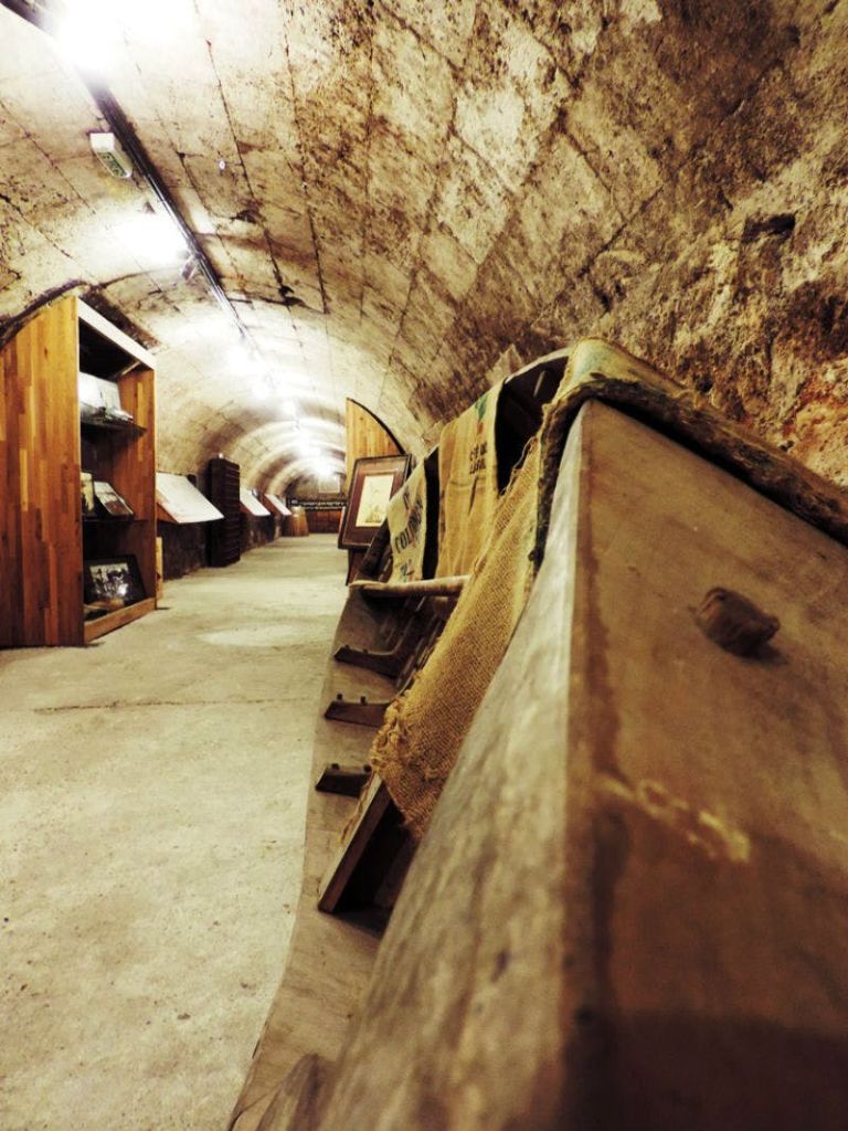 양쪽에 나무 디스플레이가 있는 지하 터널, 낡은 나무 통, 삼베 자루가 벽을 둘러싸고 있습니다.