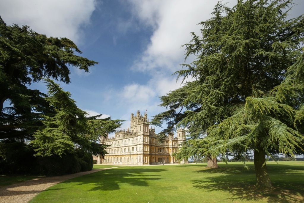 부분적으로 흐린 하늘 아래 푸른 잔디밭과 높은 나무로 둘러싸인 포탑이 있는 유서 깊은 성 모양의 건물입니다.