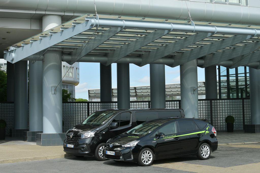 현대적인 강철 및 유리 캐노피 구조 아래 밴과 자동차를 포함한 두 대의 검은색 주차 차량.