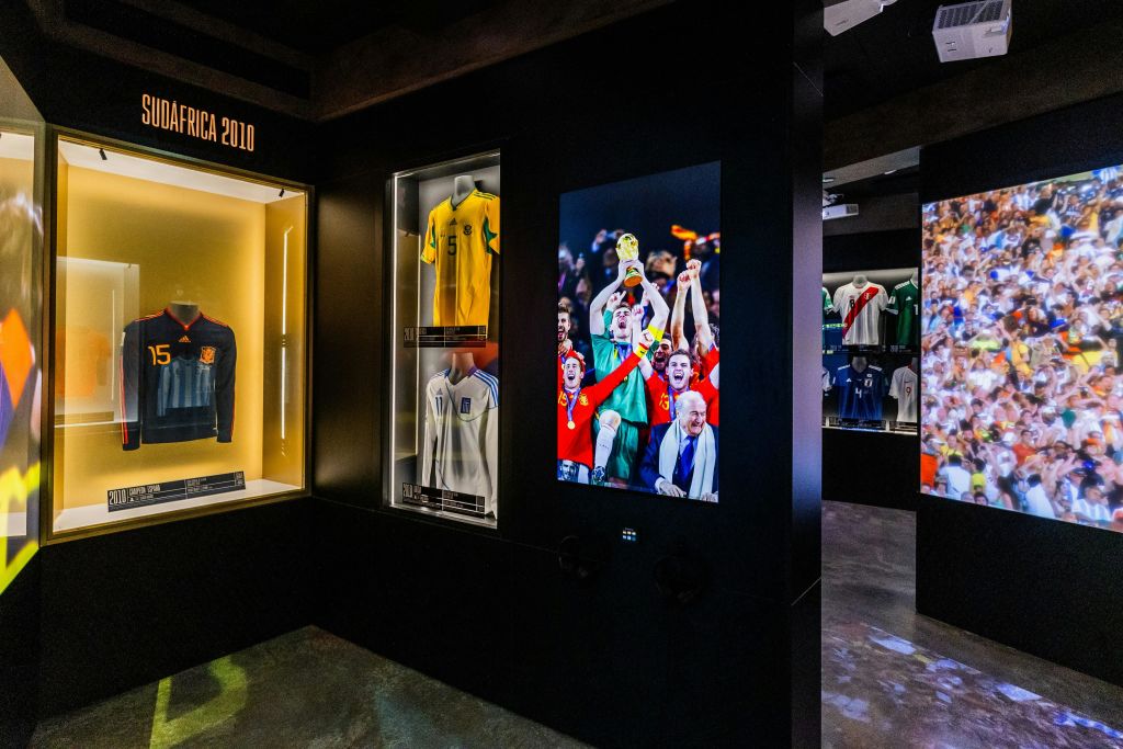 유리 케이스에 축구 유니폼을 넣은 박물관 디스플레이와 트로피를 들고 축하하는 팀을 보여주는 화면.