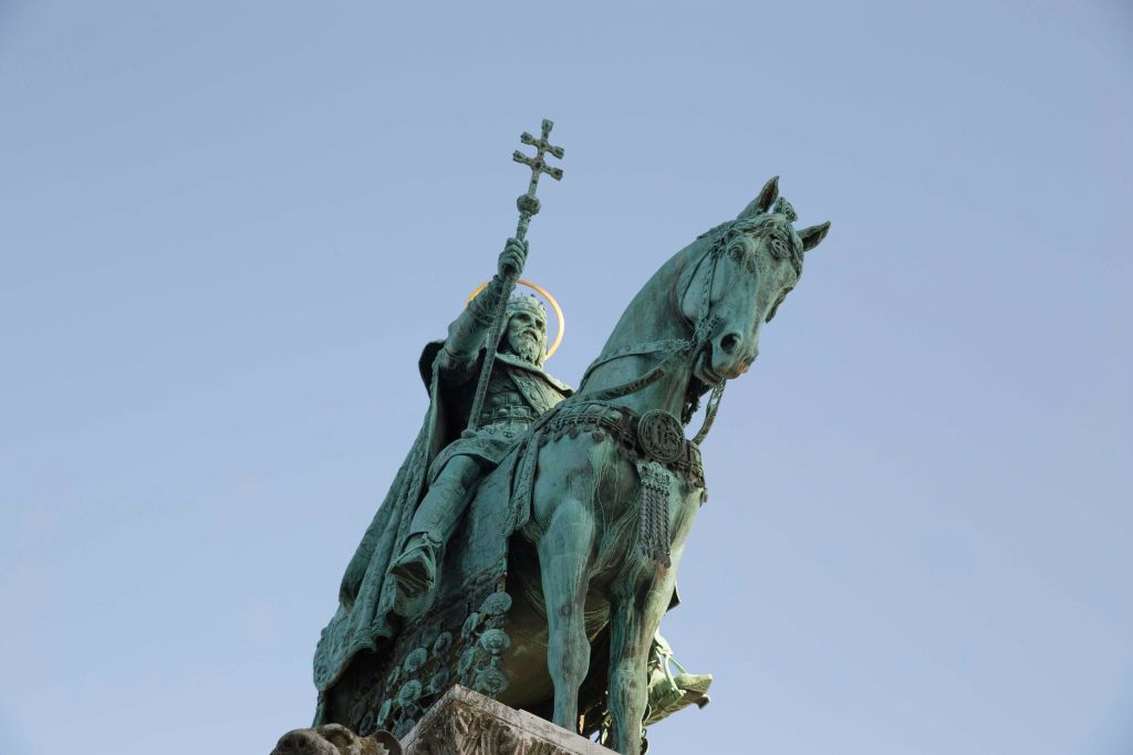 맑고 푸른 하늘을 배경으로 석재 받침대에 십자가를 들고 있는 수염이 달린 모습의 청동 승마 동상.