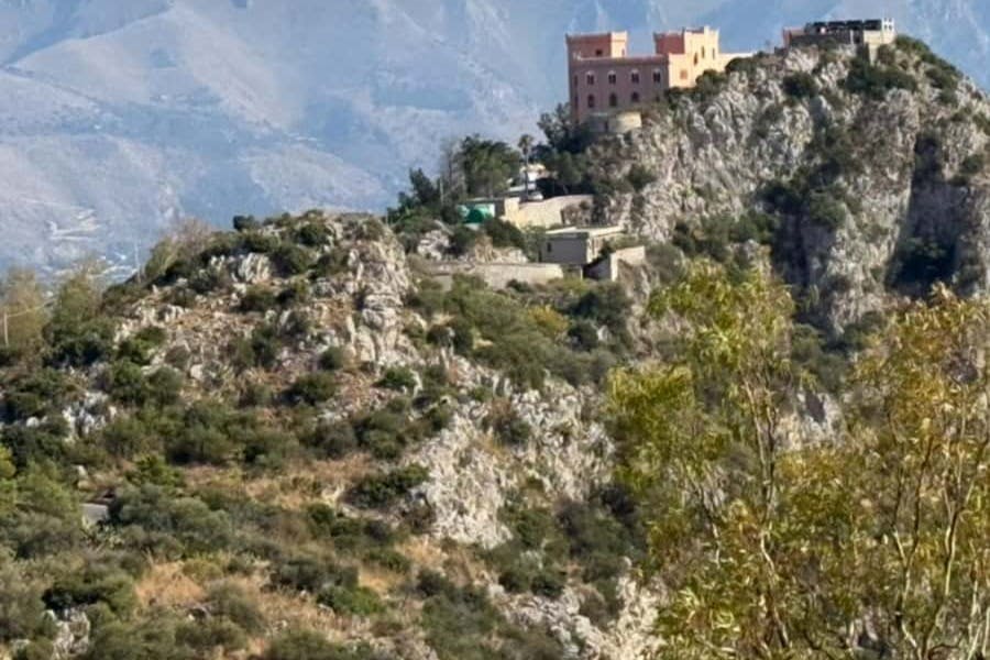 암석 지형과 녹지가 있는 언덕 꼭대기에 분홍색과 주황색 구조를 포함한 여러 건물이 있습니다.