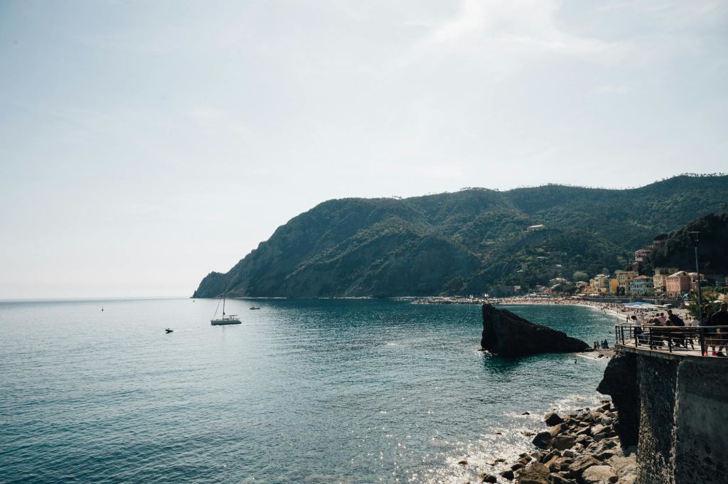 고요한 푸른 물, 요트, 바위 해안, 푸른 언덕을 배경으로 맑은 하늘 아래 펼쳐지는 고요한 해안 풍경.