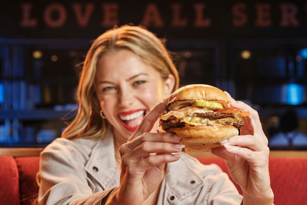 레스토랑에서 미소를 짓고 양손으로 햄버거를 들고 있는 사람.