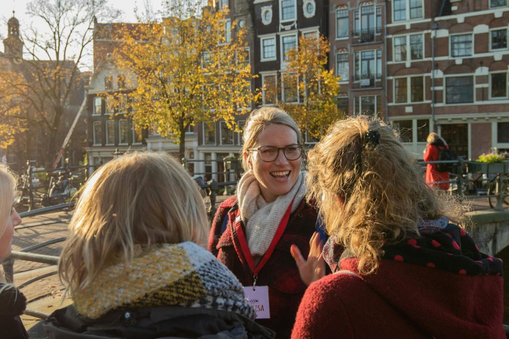 화창한 날씨에 단풍, 벽돌 건물, 나무를 배경으로 세 사람이 밖에서 이야기를 나누고 있습니다.