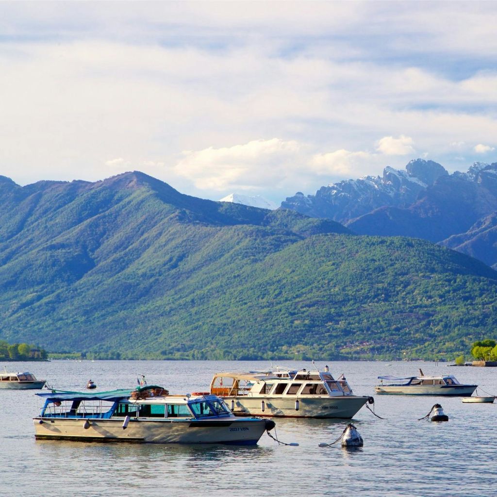 푸르고 숲으로 뒤덮인 산과 부분적으로 흐린 하늘을 배경으로 한 잔잔한 호수에 여러 척의 보트가 정박해 있습니다.