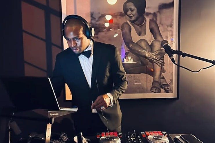 헤드폰이 달린 정장 차림의 DJ가 믹서를 작동합니다. 한 여성의 흑백 사진이 배경으로 보입니다.