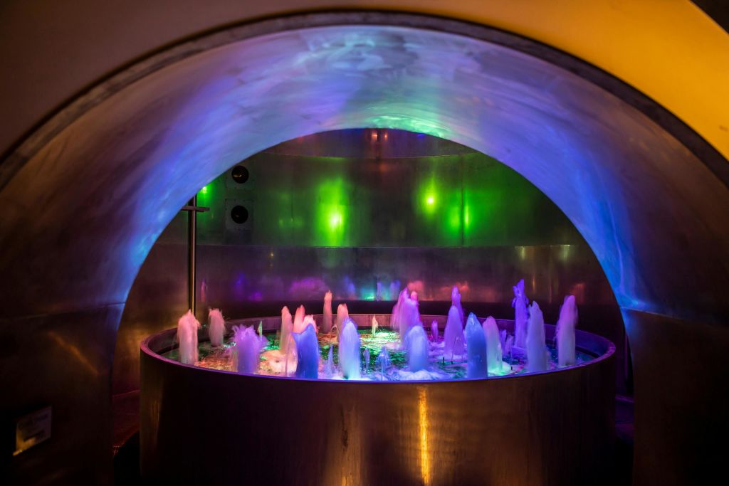 금속 배경으로 워터젯을 비추는 다색 조명이 있는 원형 실내 분수대입니다.