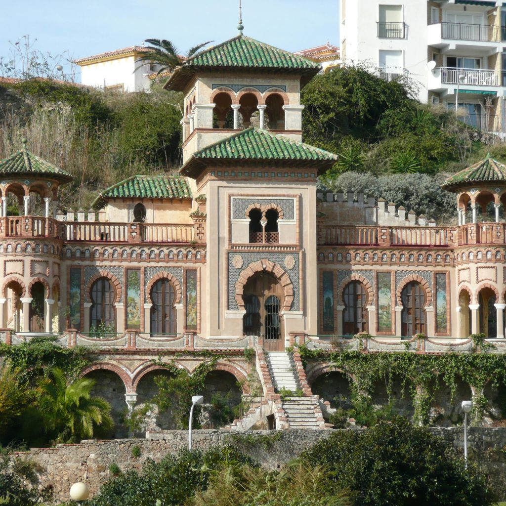아치형 창문과 녹색 타일 지붕을 갖춘 화려한 다층 건물로, 초목으로 둘러싸여 있으며 현대적인 건물과 인접해 있습니다.