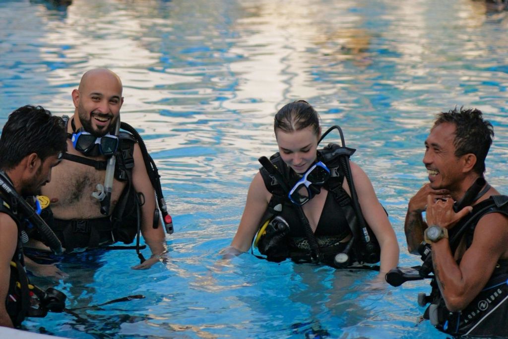 수영장에서 스쿠버 다이빙 장비를 착용한 세 사람이 미소를 지으며 다이빙을 준비하고 있습니다.