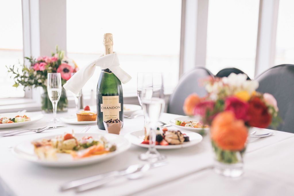 샹동 샴페인 병, 유리잔, 고급 음식 접시, 다채로운 꽃 장식이 있는 우아한 테이블 세팅.
