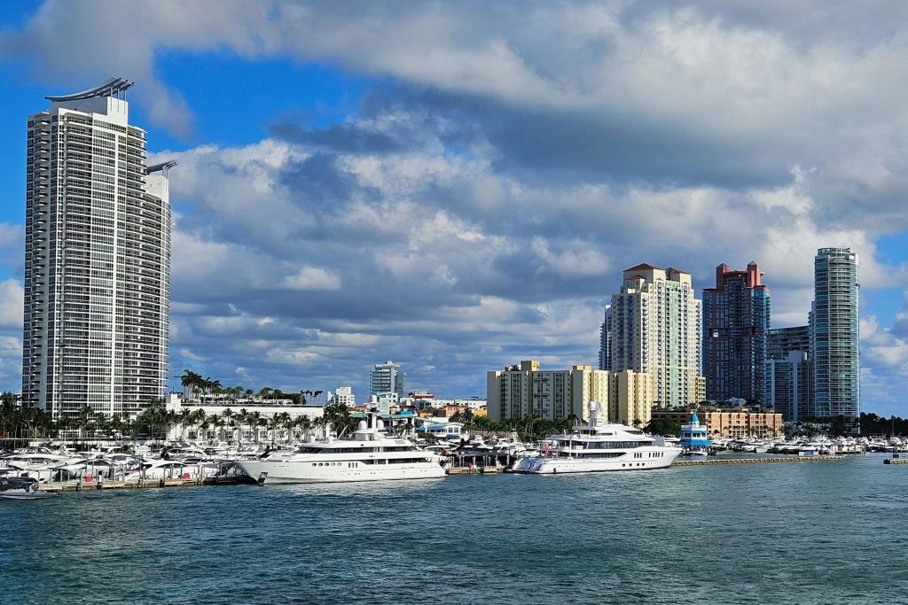 부분적으로 흐린 하늘 아래 높은 건물을 배경으로 여러 요트가 물가를 따라 정박했습니다.