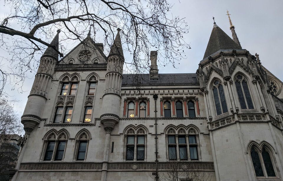 아치형 창문과 높은 첨탑이 있는 고딕 양식의 건물 정면은 아래에서 볼 수 있으며, 부분적으로는 맨 나뭇가지로 가려져 있습니다.