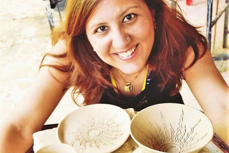 카메라를 보며 웃고 있는 한 여성이 장식된 도자기 그릇이 놓인 테이블에 기대어 앉아 있습니다.