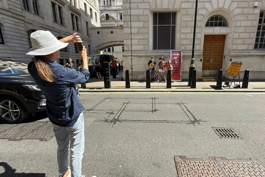 햇살 가득한 도시 거리의 빨간색 전화 부스 근처에서 포즈를 취하는 단체 사진을 찍고 있는 사람이 모자를 쓰고 있습니다.