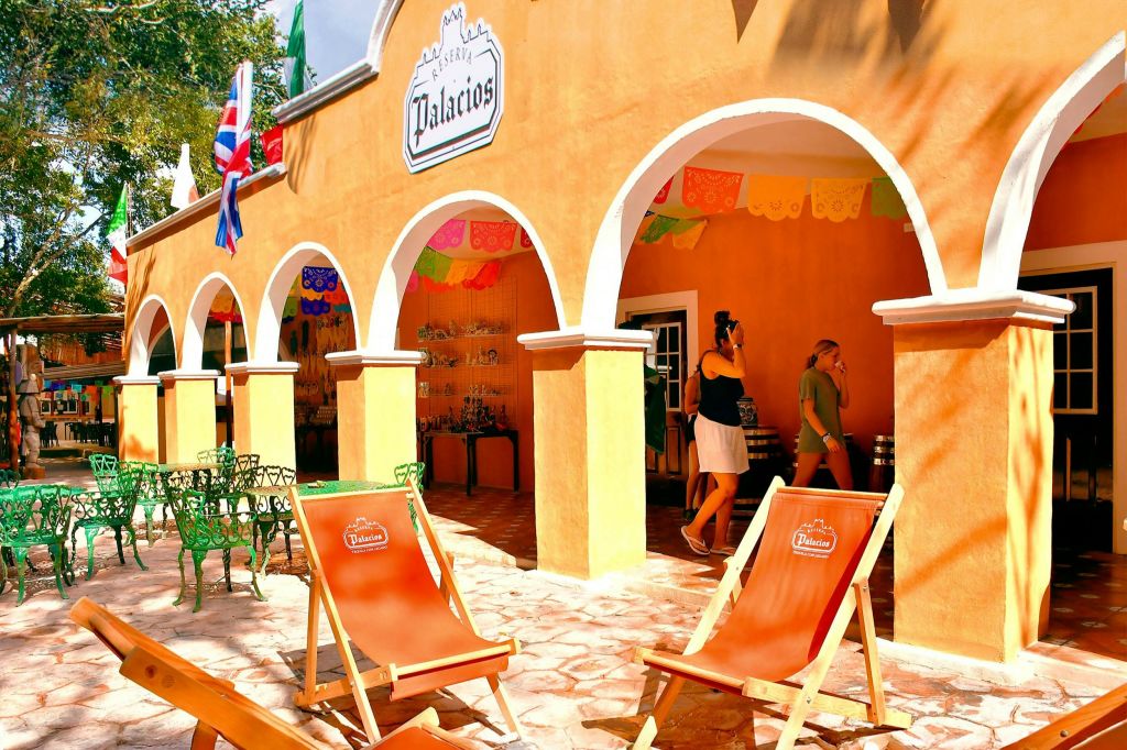 주황색 데크 의자와 아치형 출입구, 다채로운 배너, 내부 상점이 있는 건물이 있는 야외 좌석.