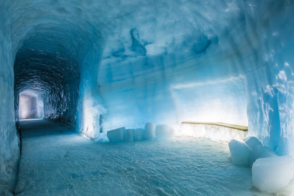 푸른빛이 감도는 벽과 바닥에 놓인 얼음 덩어리, 인공 조명이 비추는 나무 난간이 있는 얼음 동굴.