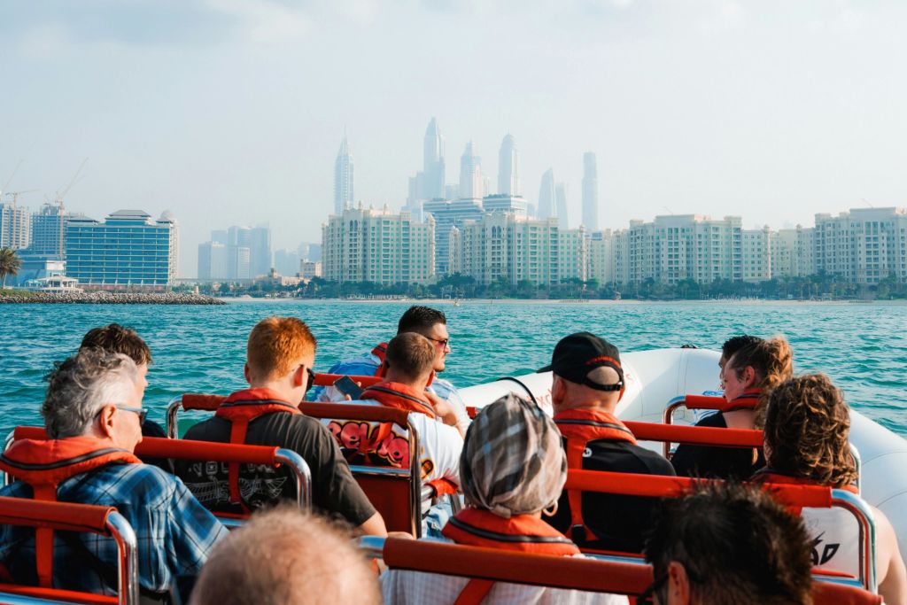 높은 건물을 배경으로 한 도시의 스카이라인이 있는 보트에서 구명조끼를 입은 사람들의 모임.