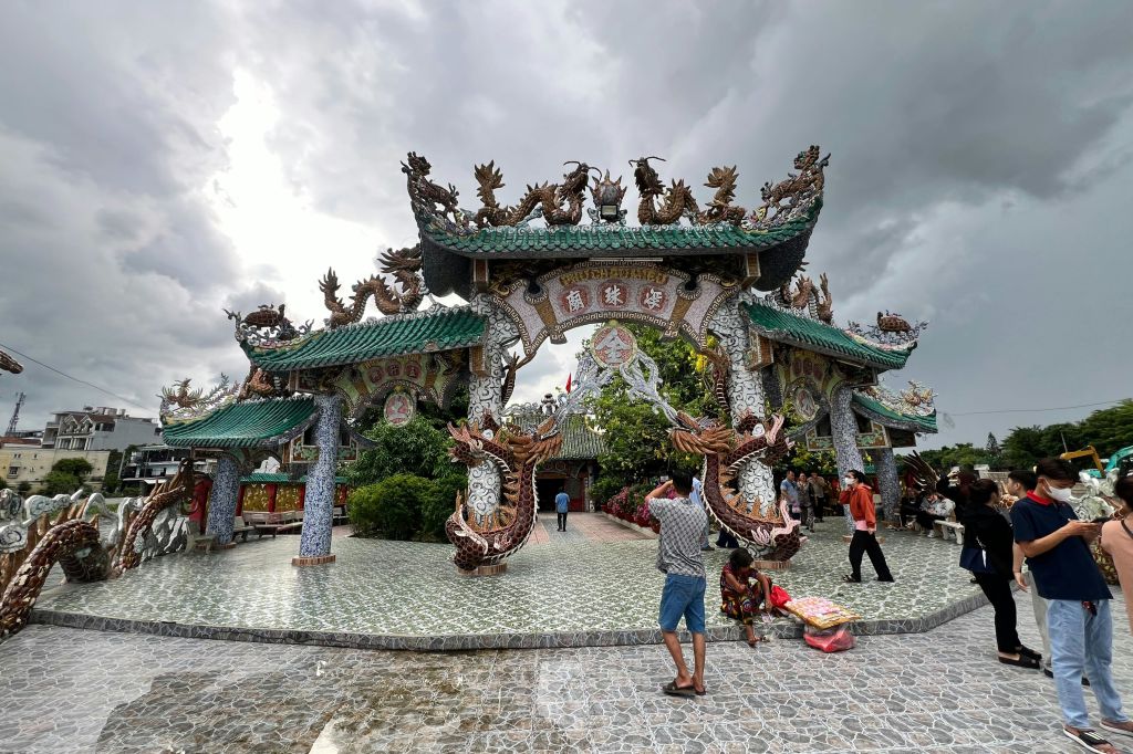 구름이 낀 하늘 아래, 걷고 사진을 찍는 사람들과 함께 타일로 둘러싸인 공간에 드래곤 장식을 한 화려한 문.