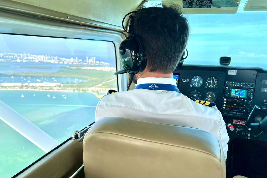 조종석 창문을 통해 보이는 해안선과 도시 풍경이 보이는 비행기를 타고 헤드폰을 착용한 조종사.