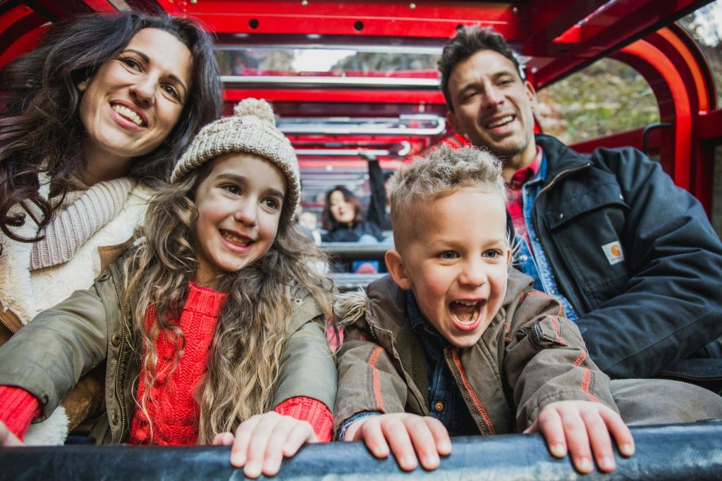 4인 가족의 미소가 놀이 기구에 앉아 있습니다. 어머니와 딸은 왼쪽에, 아버지와 아들은 오른쪽에 있습니다.