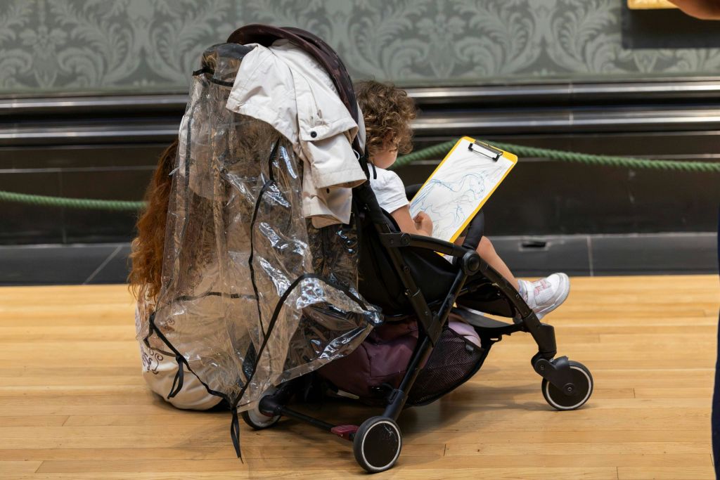 유모차에 탄 어린이가 투명 레인 커버로 덮인 클립보드에 그림을 그리고 있습니다.