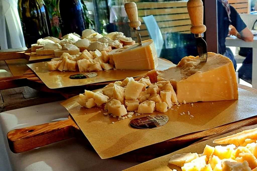 테이블 위에 칼이 박혀 있는 도마 위에 치즈 덩어리가 놓여 있습니다. 배경에는 의자와 녹지가 있습니다.