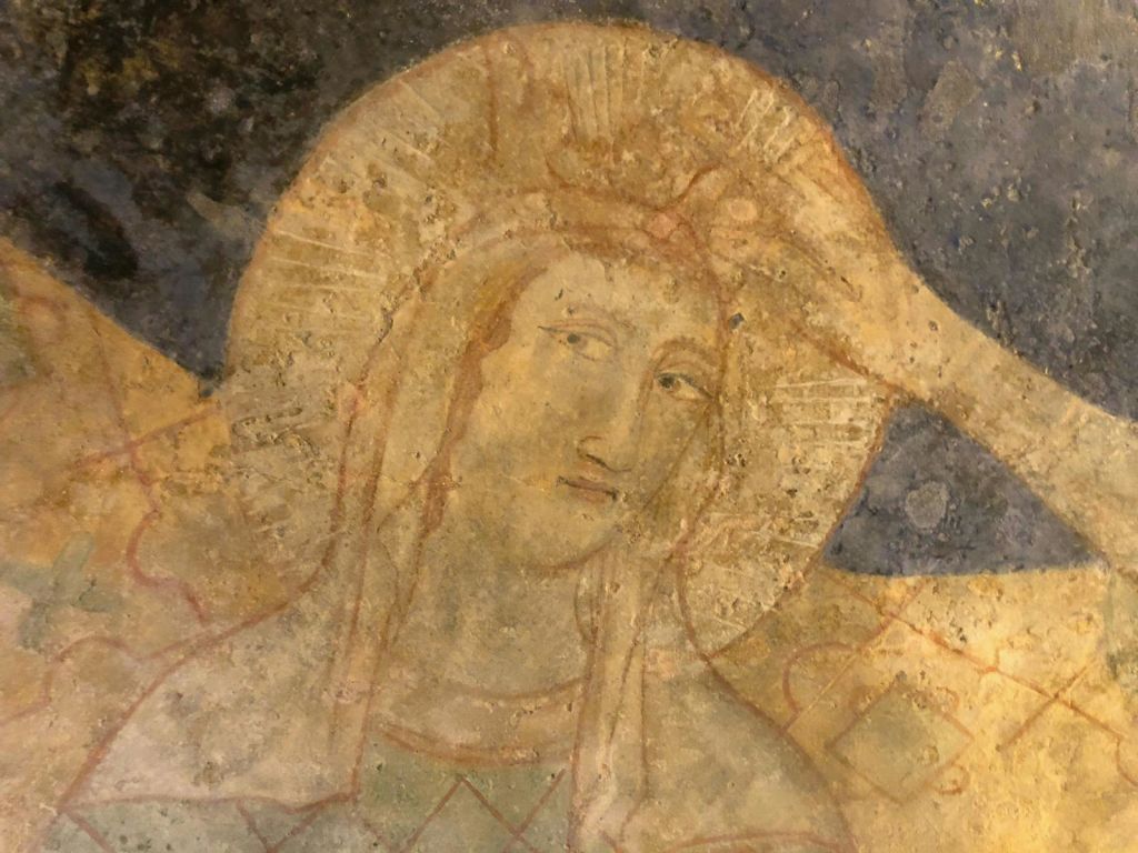 빛나는 후광이 있는 고요한 형상을 묘사한 고대 프레스코화로, 질감이 있고 풍화된 배경에 약간 낡고 세팅되어 있습니다.