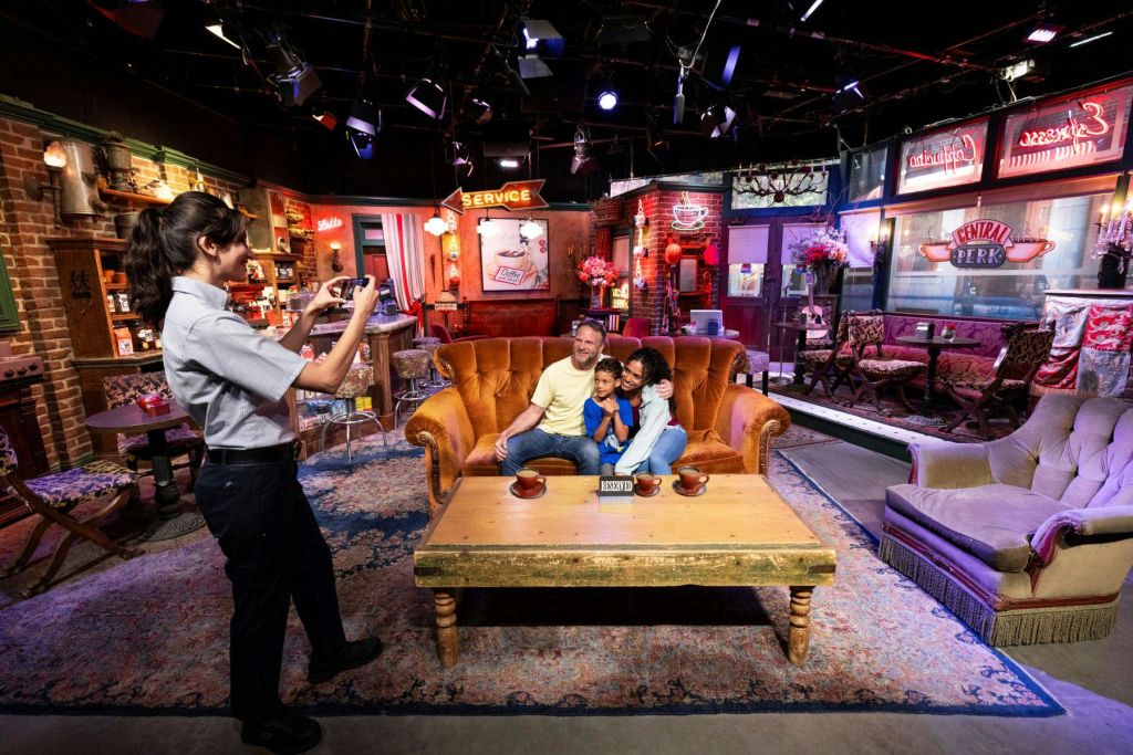 한 가족이 카페 세트의 주황색 소파에서 사진을 찍는 동안 누군가가 카메라를 들고 서서 사진을 찍고 있습니다.