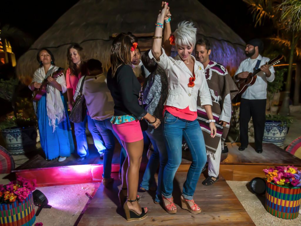 밤에 기타리스트를 배경으로 무대에서 춤을 추는 사람들. 흰 머리카락을 한 여성이 팔을 들어 올리고 있습니다.