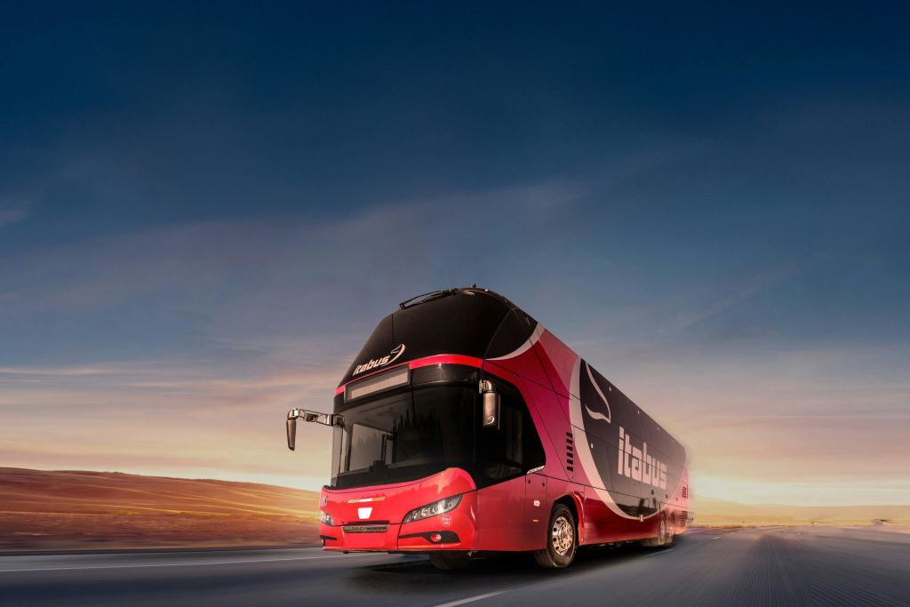 해 질 녘 도로를 달리는 빨간색과 검은색의 이층버스. 맑은 하늘을 배경으로.